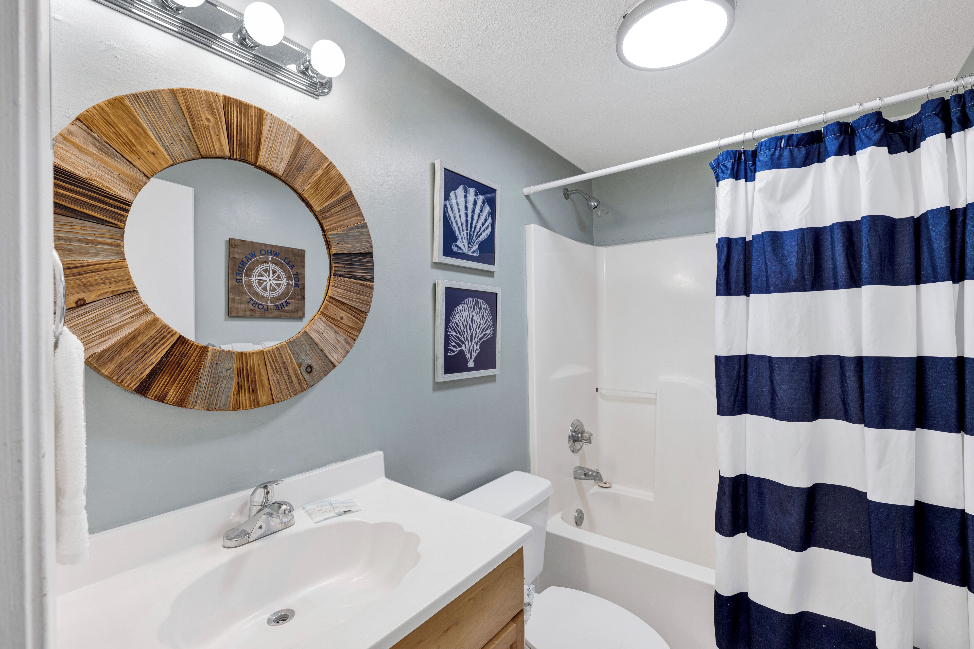 A bathroom with a round mirror, a white sink, a toilet, and a shower curtain.