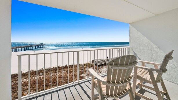 Ein Balkon mit Blick auf Strand und Steg. Ein Holz-Adirondack-Sessel und ein kleiner Tisch sind vorhanden.