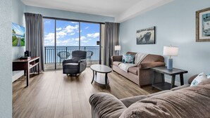 Une chambre d’hôtel avec un balcon, un canapé, une chaise, une petite table et un téléviseur.