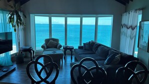 A spacious living room with a large window overlooking the sea, a comfortable sofa, and a television.
