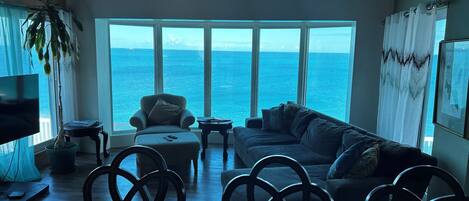 A spacious living room with a large window overlooking the sea, a comfortable sofa, and a television.