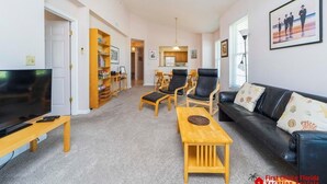 Ein Wohnzimmer mit Fernseher, Couchtisch aus Holz, schwarzem Ledersofa und Bücherregal.