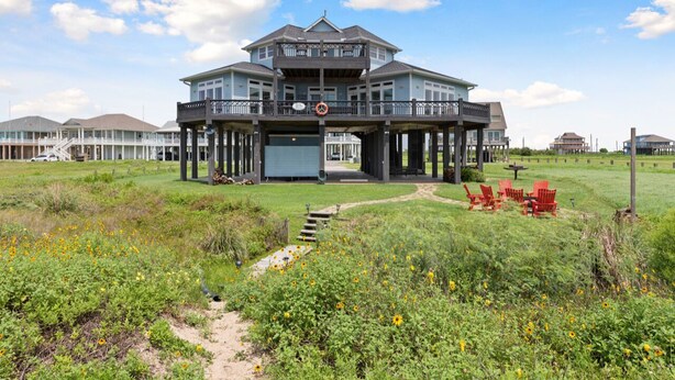 A large two-story house with a balcony, surrounded by a grassy area with yellow flowers. - WOW (Wade on the Water) - Amazing Beachfront with all the extras! (Crystal Beach)