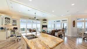 A spacious kitchen with a large island, dining area with chairs, and a view of the city through large windows. - WOW (Wade on the Water) - Amazing Beachfront with all the extras! (Crystal Beach)