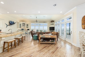 A spacious kitchen with a bar area, wooden flooring, and a view through large windows.
