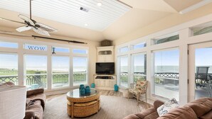 A spacious living room with a ceiling fan, large windows, a television, and a comfortable seating area. - WOW (Wade on the Water) - Amazing Beachfront with all the extras! (Crystal Beach)