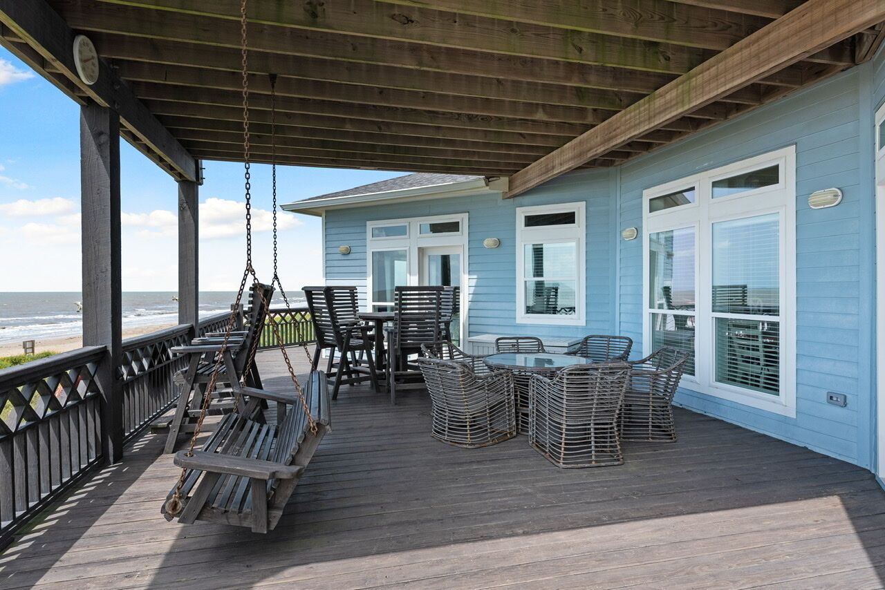 Eine Holzterrasse mit Korbmöbeln, einer Schaukel und Blick auf das Meer.