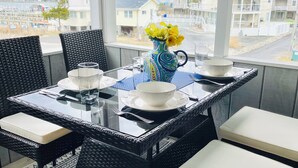 A balcony with a table set for two, featuring a vase with yellow flowers, a glass, and a bowl.