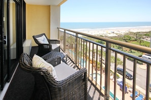 Enjoy the ocean view from this balcony with wicker furniture and a pool in sight.