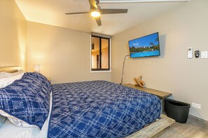 Un dormitorio con cama, ventilador de techo, ventana, televisor y termostato instalado en la pared.