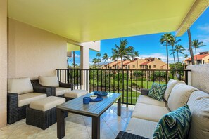 A balcony with wicker furniture, a table, and a view of palm trees and buildings. - Kamaole Sands #7-305 Inner Court, Large Lanai, Near Beach, A/C, Hot Tub! (Kihei)