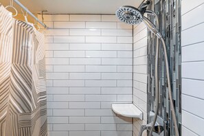 Eine Dusche mit Duschbrause, einer weiß gefliesten Wand und einem Duschkorb.