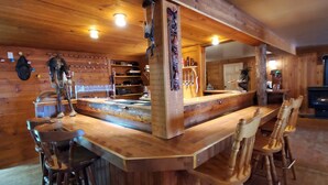 Een houten bar met een hoge toonbank, barstoelen en een rustiek interieur met houten wanden en plafond.