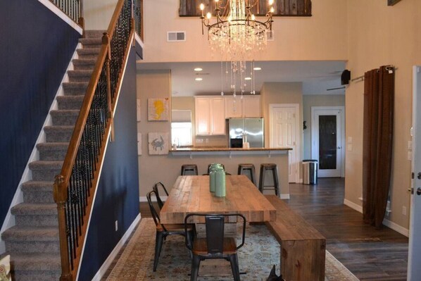 A spacious dining area with a wooden table and chairs, a chandelier, and a staircase with a wooden railing.