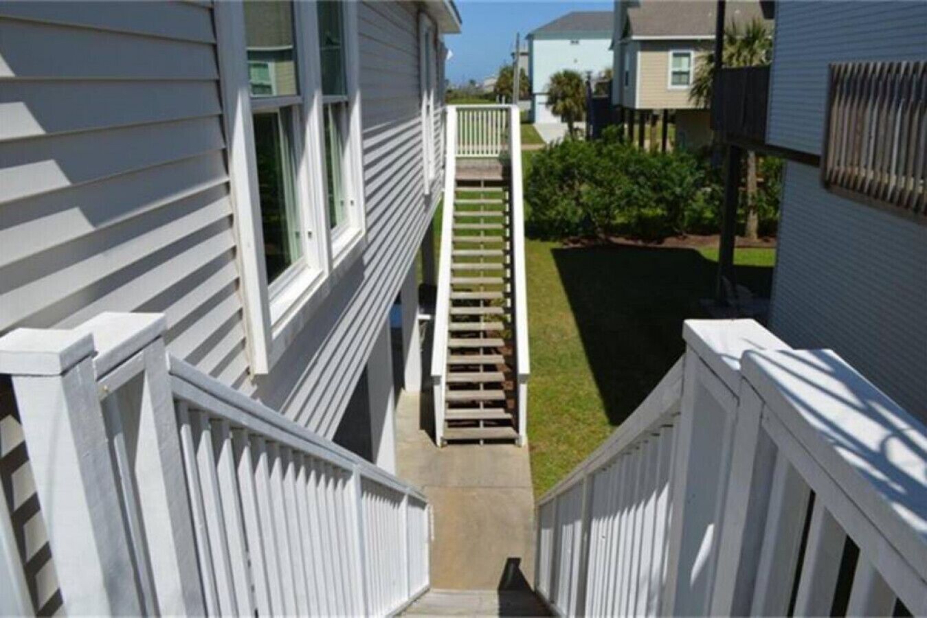 A residential building with a central staircase leading to a front door, surrounded by a white picket fence and a well-maintained lawn.
