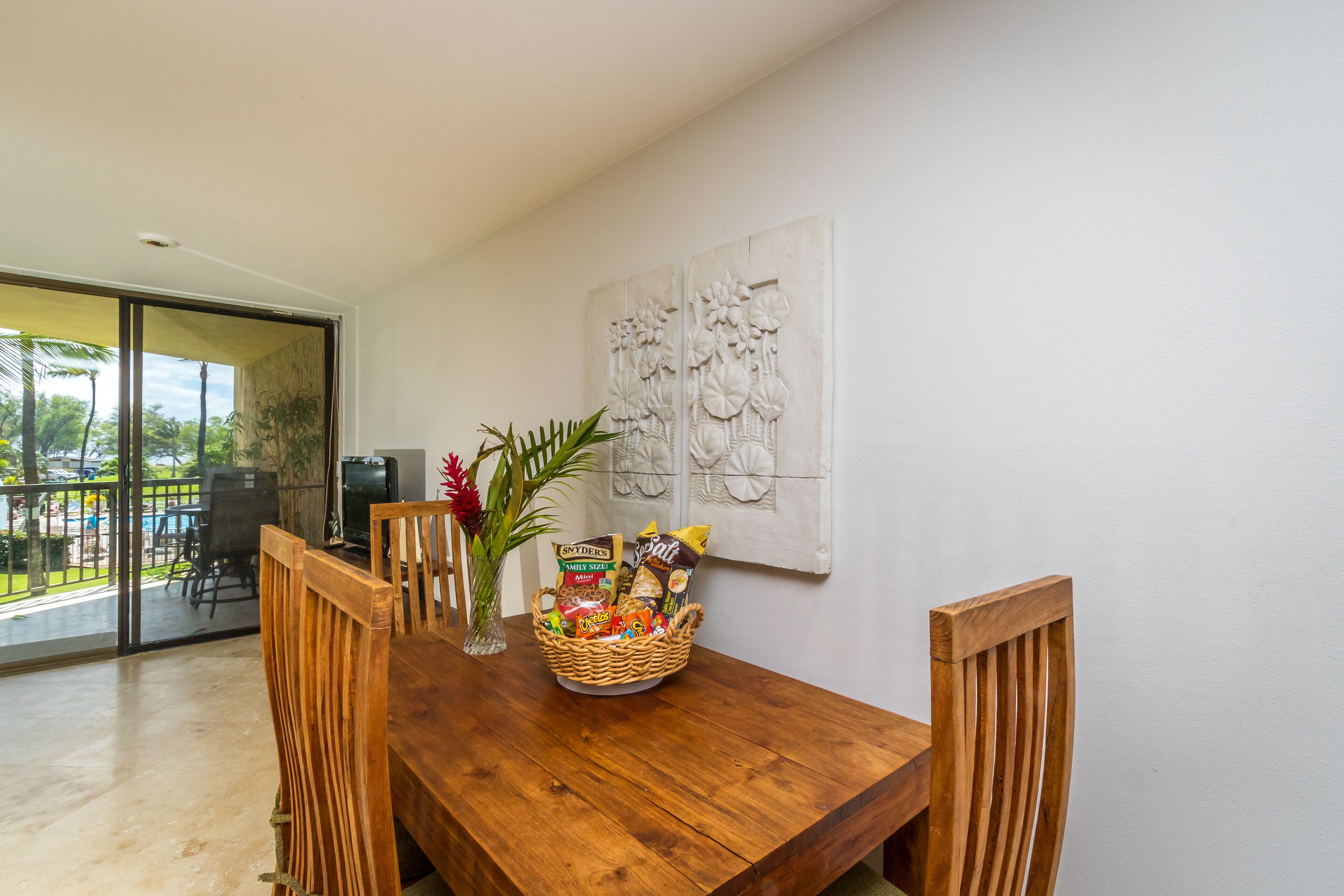 A wooden dining table with a basket of snacks and a vase with a plant.