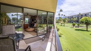 A modern hotel room with a balcony, large windows, and a view of a well-maintained lawn and building. - OCEANFRONT CONDO MAUI SUNSET#215-A, SLEEPS 4 (Kihei)