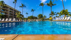 A swimming pool with lounge chairs and palm trees, surrounded by a hotel building. - OCEANFRONT CONDO MAUI SUNSET#215-A, SLEEPS 4 (Kihei)