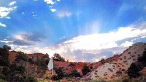Campo de golf con un mástil de bandera en primer plano y montañas al fondo.