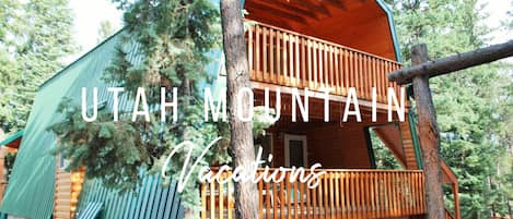 A wooden cabin with a balcony, surrounded by trees.