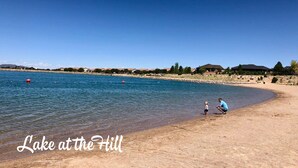 Una playa con un lago azul cristalino, algunos boyas rojas y algunas personas. Se lee el texto 'Lake at the Hill'.