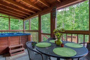 A covered outdoor area with a wooden deck, a hot tub, and a table set for dining.