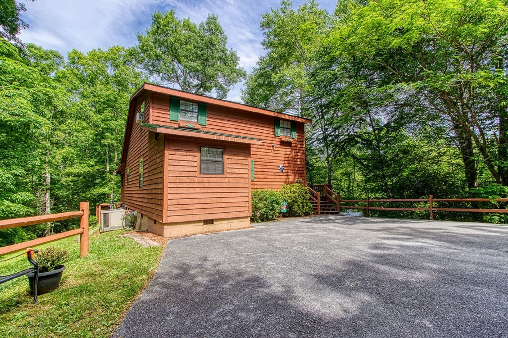 A small wooden cabin with a single window and a door, surrounded by lush greenery and a wooden fence.