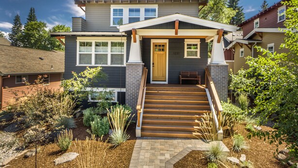 A modern two-story house with a front porch, a wooden staircase, and a well-maintained garden.