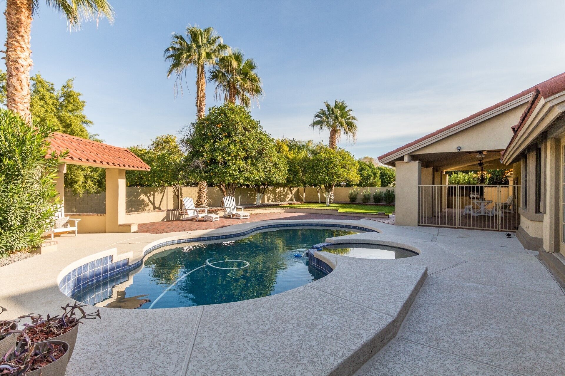 A swimming pool with a curved design, surrounded by a patio area with lounge chairs and a covered seating area.