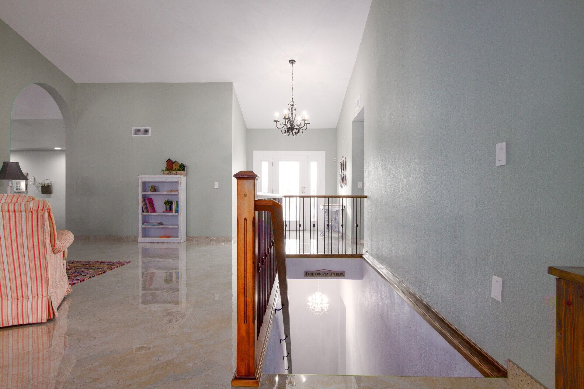 Un vaste hall d’entrée doté d’un sol en marbre, d’un escalier avec une rampe en bois et d’un lustre.