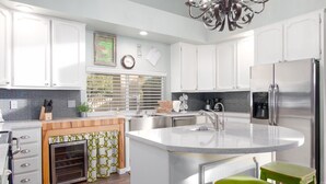 Una cocina moderna con armarios blancos, un refrigerador de acero inoxidable, un horno empotrado y una isla grande con un fregadero.