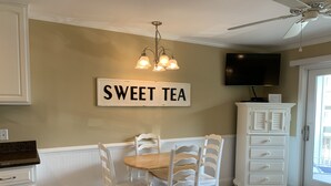 Un área de comedor con una mesa y sillas, un letrero que dice 'SWEET TEA', un ventilador de techo y un televisor en la pared.
