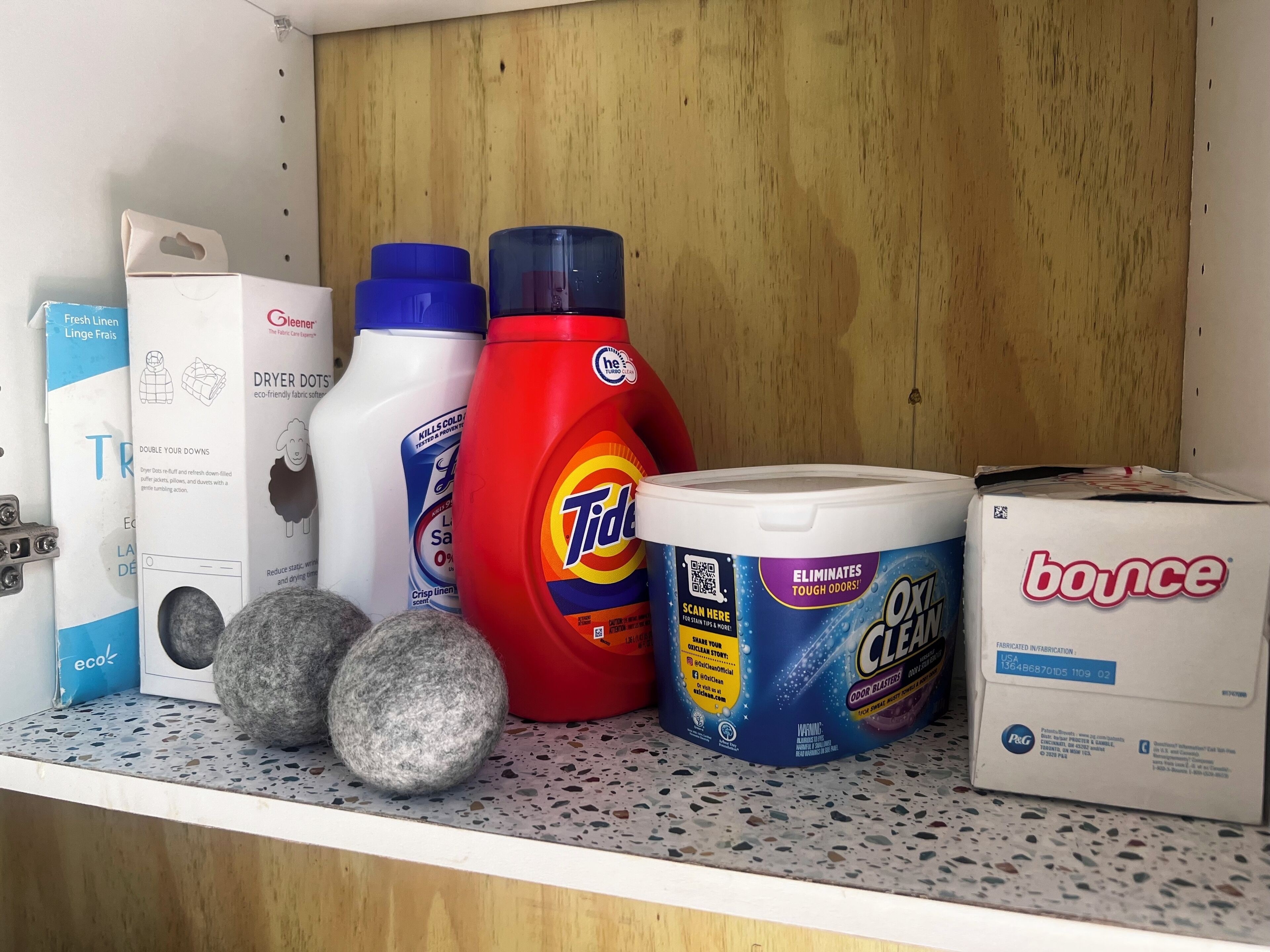 A shelf with various cleaning products including Tide, Bounce, and a container of OxiClean.
