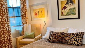 A bedroom with a bed, a chair, a window with curtains, and two framed artworks on the wall. - Tropical, private, downtown (Sarasota)
