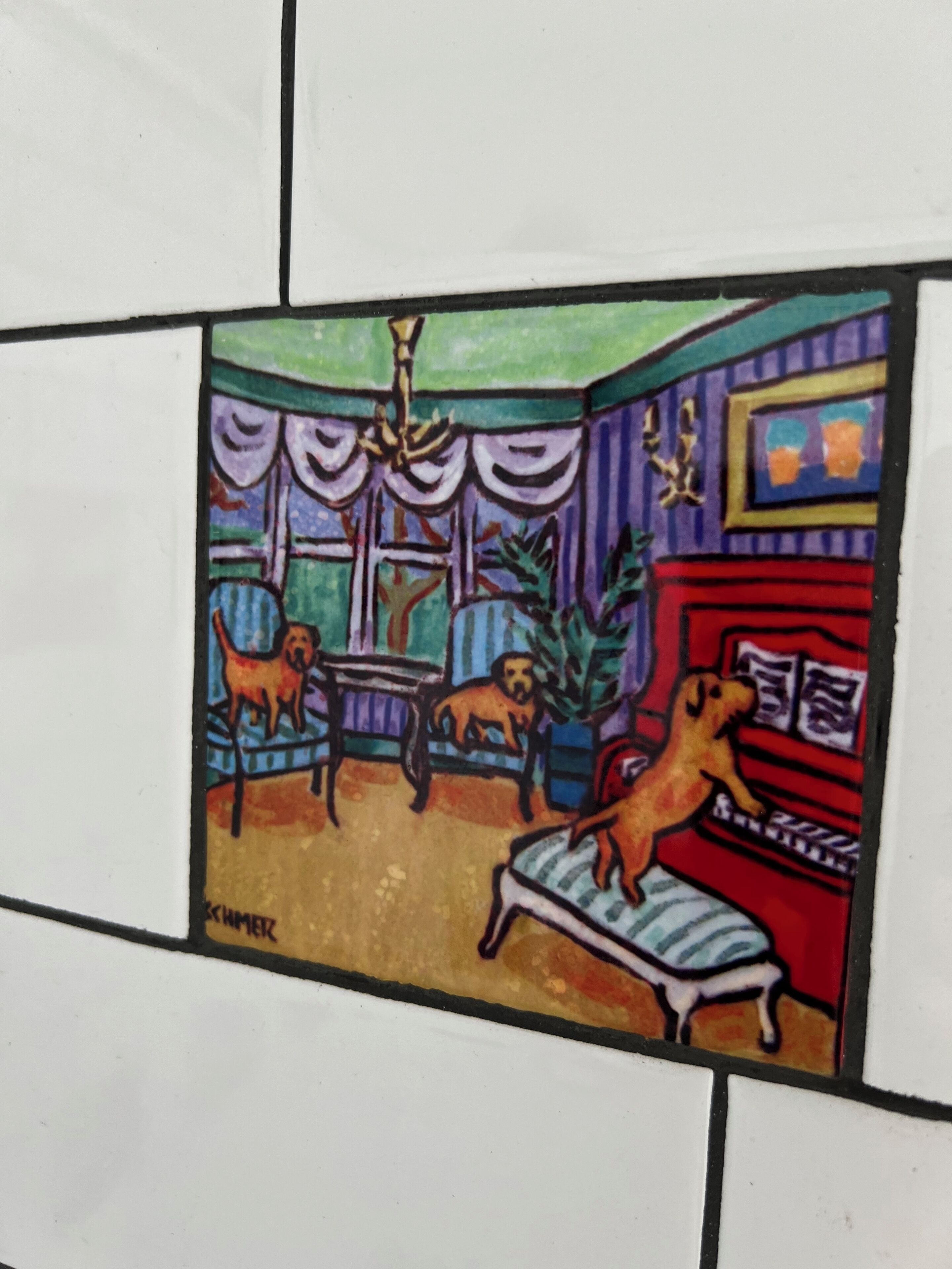 Een betegelde muur met een kleurrijk schilderij van een kamer, waarop twee honden, een tafel, stoelen en een open haard te zien zijn.