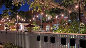 An outdoor patio area with string lights, a white picket fence, and a building in the background. - Tropical, private, downtown (Sarasota)