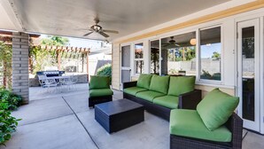 Eine Terrasse im Freien mit Grill, grünen Sitzgelegenheiten und einem Deckenventilator.