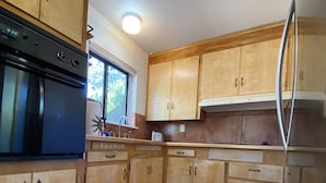 Une cuisine avec des meubles en bois, un poêle noir et une fenêtre donnant sur un paysage verdoyant.
