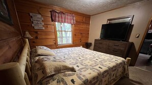 A bedroom with a bed, a dresser, a television, and a window with blinds.