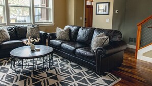 A living room with a black leather sofa, a round coffee table, and a patterned rug. - Amazing West Side * 2 King Suites * Walk Everywhere  * 8 Person Hot Tub (Bend)