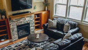 A living room with a sectional sofa, a fireplace, a TV, and a staircase. - Amazing West Side * 2 King Suites * Walk Everywhere  * 8 Person Hot Tub (Bend)