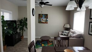 Un coin repas avec une table, des chaises et un ventilateur de plafond. On aperçoit un canapé et une lampe au fond.