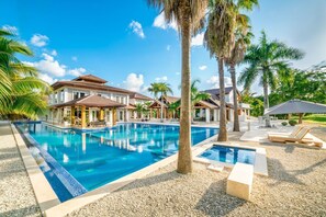 Een resort met een groot zwembad, palmbomen en een helderblauwe lucht.