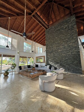 Un espacio de sala amplio con techo alto, pared de piedra y mobiliario moderno.