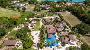 Eine Vogelperspektive zeigt ein Resort mit mehreren Gebäuden, einem zentralen Schwimmbecken und direktem Strandzugang.
