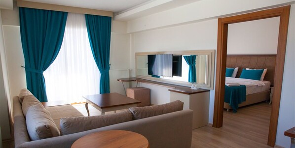 A modern hotel room with a sofa, a small table, a bed with blue pillows, and a large mirror. - Black Forest Hotel (Savsat)