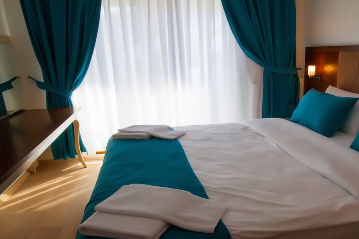 A neatly made bed with teal and white bedding, a wooden nightstand, and teal curtains.