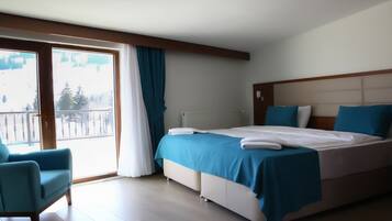 Habitación de hotel con una cama grande, una silla, vista a un paisaje nevado a través de una puerta corrediza y un radiador.