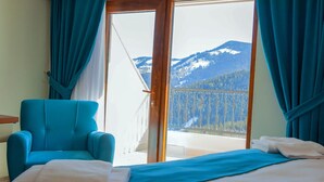 Una habitación con cama, un sillón azul y un balcón con vistas a la montaña.