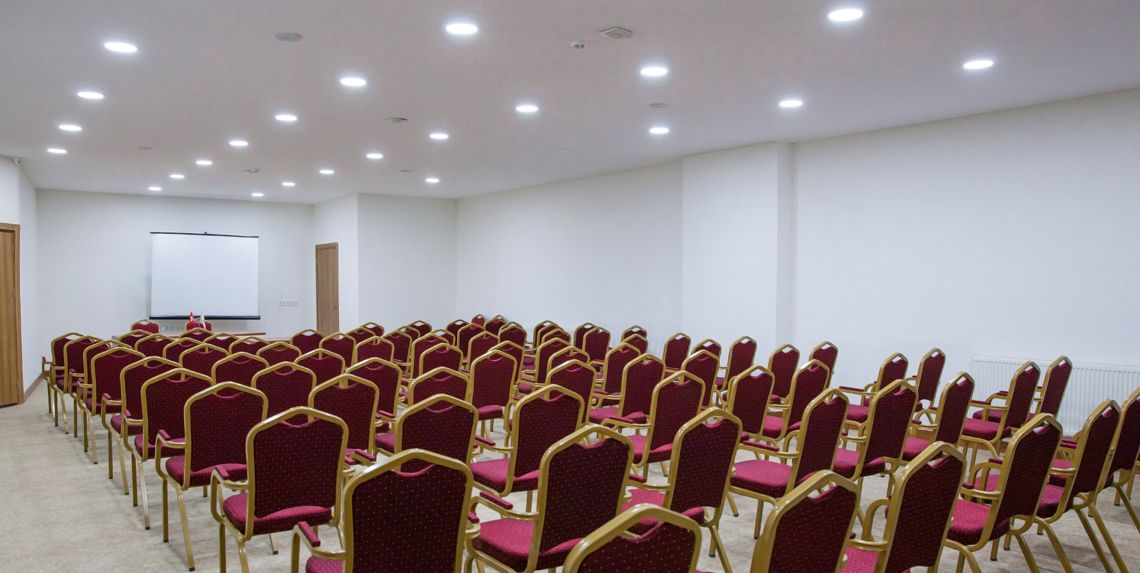 A conference room with rows of red chairs and a whiteboard at the front.